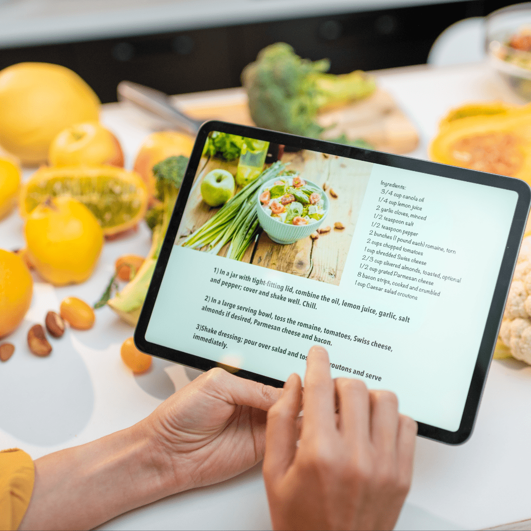 Person using tablet displaying Noory Meal Plan and Recipe platform with fresh fruits and vegetables on kitchen counter