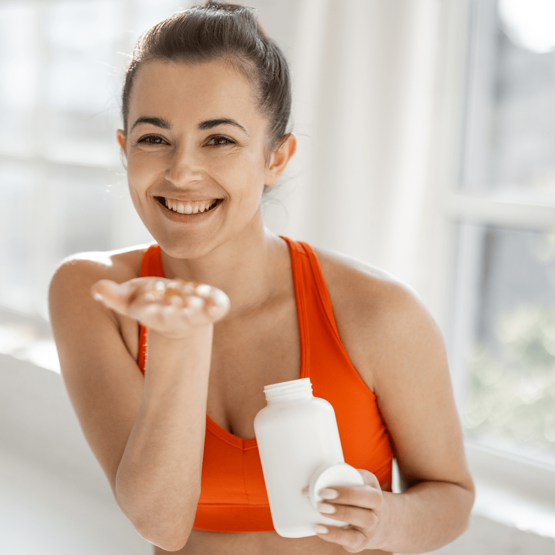 Smiling woman in orange sports bra holding white supplement bottle and offering personalised supplement advice